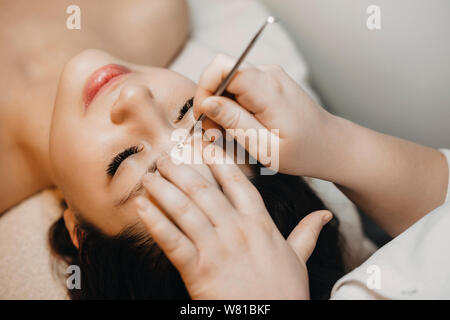 Primo piano di una bella donna appoggiata su un letto di spa con gli occhi chiusi mentre il manuale di pulizia del viso da un estetista in un centro termale. Foto Stock