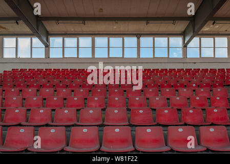 Visualizza riga di rosso sedili in plastica su terreni accidentati passo concreto piano nel vecchio vintage calcestruzzo sporco stadio strutturale senza persone. Foto Stock