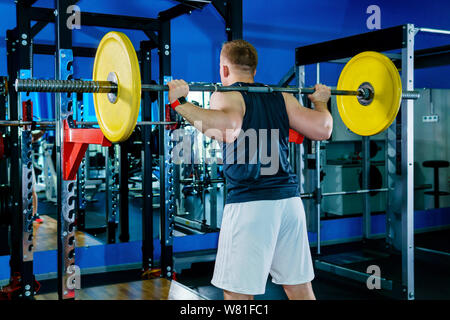 Atleta esegue uno squat barbell accanto alla macchina per pesi nella palestra Foto Stock