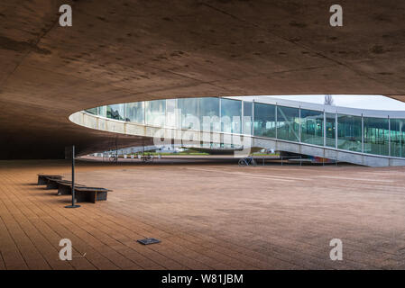 Esterno al piano terra della Rolex Learning Center (EPFL) con calcestruzzo affascinano ondulata di pavimento forato e tetto con facciata di vetro. Foto Stock