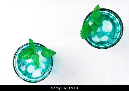 Due belle vintage occhiali turchese con bevanda fredda e cubetti di ghiaccio, decorata con fresco verde menta su marmo bianco tavola. Vista dall'alto. Foto Stock