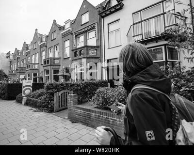Haarlem, Paesi Bassi - 16 agosto 2018: vista posteriore della donna con zaino camminando sulla piccola strada ammirando architettura olandese in bianco e nero Foto Stock