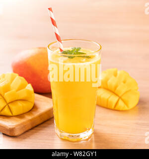 Freschi di succo di mango con bella polpa tritata carne su legno luminoso sullo sfondo della tabella. Bevanda a base di frutta tropicale di design. Close up, copia dello spazio. Foto Stock