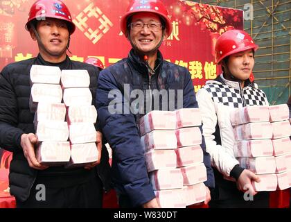 Cinese i lavoratori migranti mostrano fasci di 100-yuan RMB (Renminbi) banconote per i loro stipendi e premi di fine anno presso il cantiere per la costruzione di una vera e Foto Stock