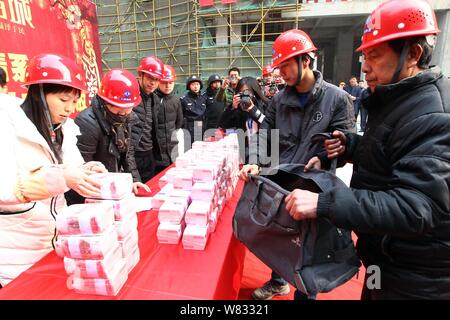 Cinese i lavoratori migranti ottenere fasci di 100-yuan RMB (Renminbi) banconote per i loro stipendi e premi di fine anno presso il cantiere per la costruzione di una vera e propria es Foto Stock