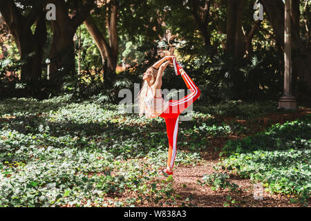 La donna a praticare lo yoga si estende nel parco, indossando activewear Foto Stock