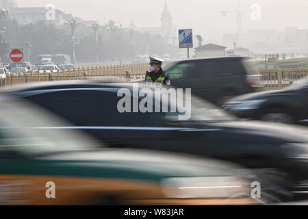 --FILE--cinese di un funzionario di polizia che indossa una maschera facciale contro l' inquinamento atmosferico dirige il traffico su una strada vicino a Piazza Tienanmen in pesanti smog a Pechino, C Foto Stock