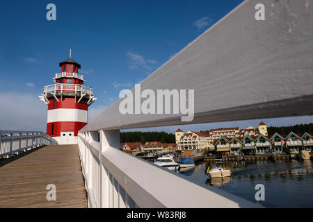 Rheinsberg, Germania. 02Aug, 2019. Il faro in harbour village di Rheinsberg, un marina con 208 Scandinavian a struttura mista in legno e muratura case vacanza e cuccette per gli appassionati di sport acquatici sul lago di Rheinsberg sul lago Meclemburgo. Sullo sfondo il Maritim Hafenhotel Rheinsberg. Credito: Jens Kalaene/dpa-Zentralbild/ZB/dpa/Alamy Live News Foto Stock