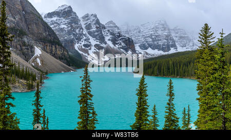 Il Moraine Lake - Una vista panoramica del Lago Moraine e le sue montagne circostanti su terreni innevati e nebbioso giorno di primavera, il Parco Nazionale di Banff, Alberta, Canada. Foto Stock