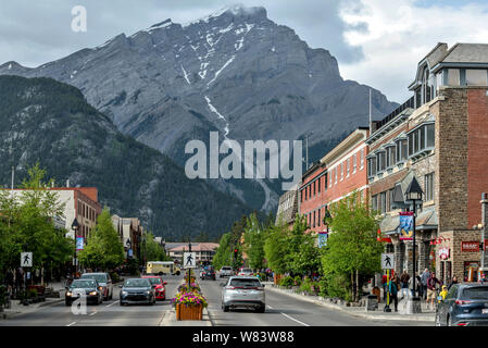 La Cascade Mountain a Banff Ave - formidabile cascata torreggiante montagna alta in corrispondenza di estremità lontana della trafficata Banff Avenue su un nuvoloso giorno di primavera nel centro cittadino di Banff. Foto Stock