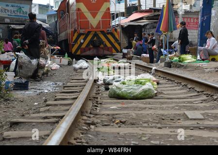 I fornitori cinesi guardare un treno merci passando attraverso un bazar lungo una ferrovia merci nel villaggio di Nanling, Zunyi city, a sud-ovest della Cina di Guizhou provi Foto Stock