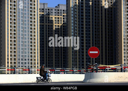 --FILE--un ciclista cavalca la sua bicicletta elettrica passato alto appartamento residenziale edifici in città Huaian, est cinese della provincia di Jiangsu, 6 ottobre 2016 Foto Stock