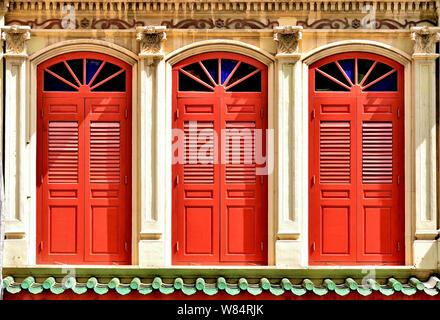 Close up vintage di finestre ad arco con antichi red persiane di legno su esterno bianco della tradizionale Peranakan di Singapore o stretto bottega cinese Foto Stock