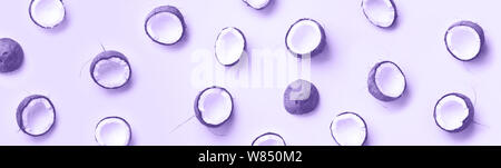 Modello con noci di cocco mature su viola alla moda colore di sfondo. Vista dall'alto. Copia dello spazio. La Pop art design, creativi concetto d'estate. La metà di noce di cocco in minimi Foto Stock