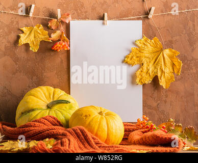 Vuoto foglio di carta bianco foglie secche appesi clothespins con zucca sciarpa sfondo marrone. Cartolina di autunno Foto Stock