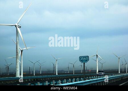 --FILE--un'auto passa da turbine eoliche in una fattoria eolica in Urumqi city, a nord-ovest della Cina di Xinjiang Uygur Regione autonoma, 17 giugno 2013. Dopo l'installazione Foto Stock