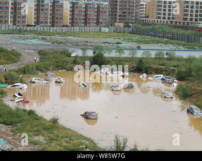 Le automobili private sono immerse in acqua dopo essere stata lavata da inondazioni causate da un acquazzone in una buca dal parcheggio in un quartiere residenziale in Foto Stock