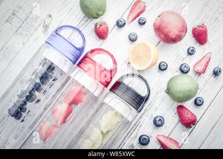 Infusa detox acqua in bottiglie con frutta fresca e bacche su sfondo di legno, vista dall'alto Foto Stock