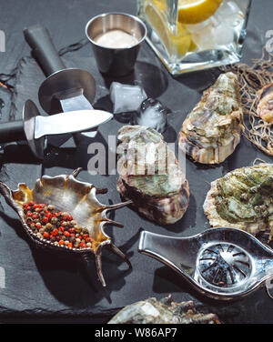 Ostriche sulla lastra di pietra con ghiaccio, limone, pesca net, il pepe e il coltello. Foto Stock