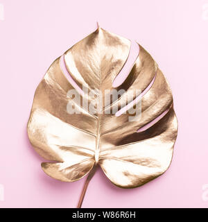 Floral stile minimal concetto. Estate esotici trend. Golden Palm tropicale monstera foglia sul rosa pastello colore di sfondo. Lucido e sparkle design, fashi Foto Stock