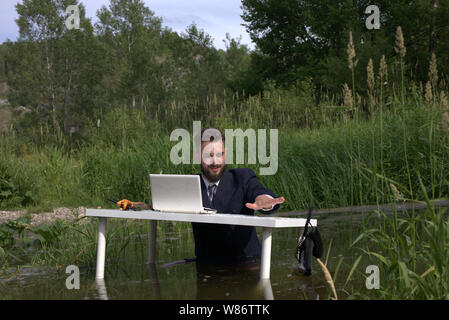 Lazy giovane uomo millenario stanchi di noioso lavoro. Si sente stressante e vuole scappare di casa. Getta un telefono in acqua in una palude. Foto Stock