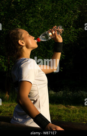 Ragazza dopo la riproduzione di sport nel parco togliere la sete beve l'acqua dalla bottiglia Foto Stock