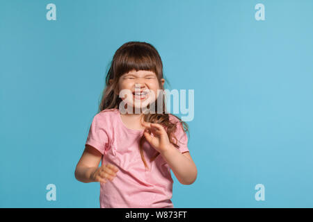 Bellissima bambina indossa in una t-shirt rosa è in posa contro un blu di sfondo per studio. Foto Stock