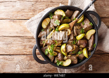 Prodotti alimentari tedeschi fritto di fegato di manzo con mele verdi e cipolle di close-up in una padella sul tavolo. parte superiore orizzontale vista da sopra Foto Stock