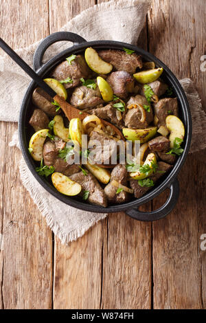 Prodotti alimentari tedeschi fritto di fegato di manzo con mele verdi e cipolle di close-up in una padella sul tavolo. Verticale in alto vista da sopra Foto Stock