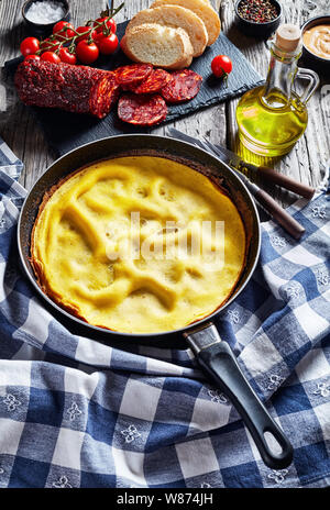 Frittata di caldo in una padella, piccante a fette di carne di maiale salsiccia, il pane e i pomodori su una scheda di ardesia su un tavolo di legno con carta asciugatutto, vista verticale da Foto Stock