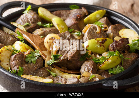 Fritto speziato fegato di manzo con mele e cipolle close-up in una padella sul tavolo orizzontale. Foto Stock