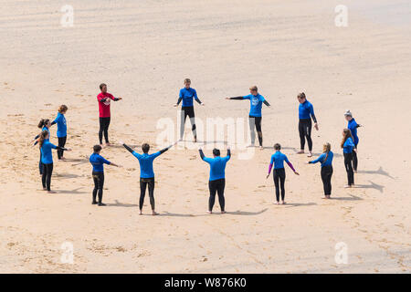 I surfisti principianti in fase di riscaldamento prima di una lezione di surf sulla grande Gt. Western Beach in Newquay in Cornovaglia. Foto Stock