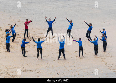 I surfisti principianti in fase di riscaldamento prima di una lezione di surf sulla grande Gt. Western Beach in Newquay in Cornovaglia. Foto Stock