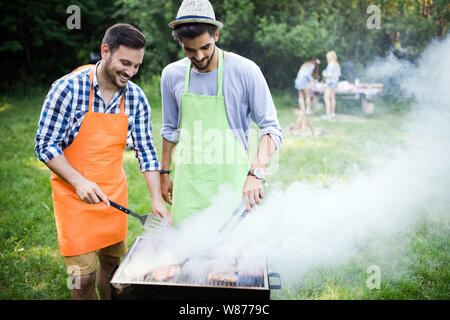 Gruppo di persone felici intorno permanente grill, chat, bere e mangiare. Foto Stock