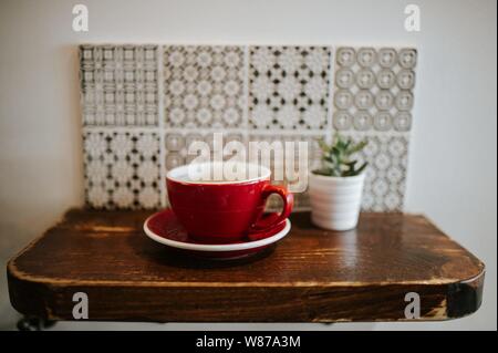 Primo piano di una tazza di ceramica rossa e di un fiore pentola su una piccola superficie di legno Foto Stock