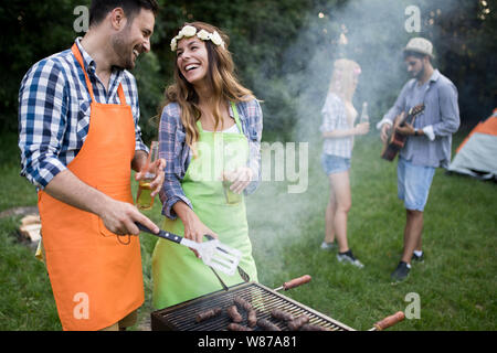 Coppia giovane con amici sorrisi e fare barbecue arrosto in campeggio Foto Stock