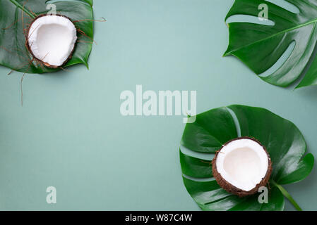 Fresche e mature noci di cocco, palma tropicali e foglie di monstera su sfondo verde con copia spazio. Vista dall'alto. Estate Concetto, layout creativi. Foto Stock