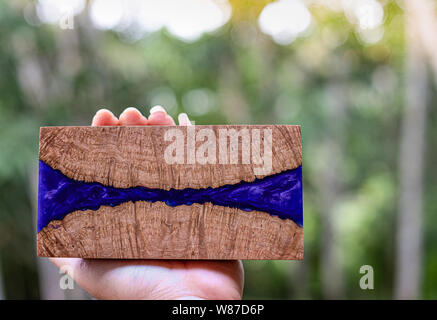 Mano che tiene la colata di resina epossidica persimmon stabilizzante radica di legno arte astratta sfondo Foto Stock