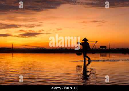 Una donna cestello porta sulla spalla e la preparazione per la raccolta di nuove sale a sunrise in Hon Khoi campo sale, Nha Trang Provincia, Vietnam Foto Stock