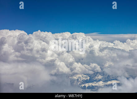 Vista aerea di un aeroplano finestra. Cime coperte di neve, cielo blu e nuvole soffici. Foto Stock