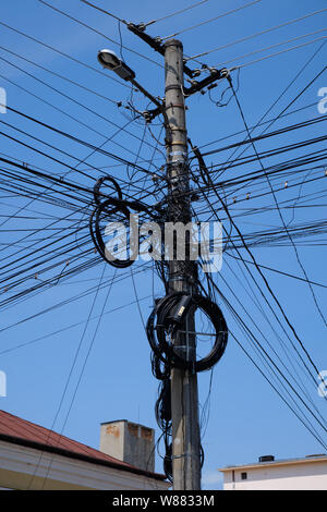 Affogate i fili elettrici in pole contro il cielo blu. Complessa rete di sopra di terra in Romania Foto Stock