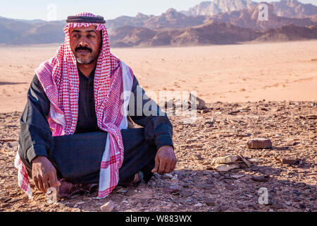 Un beduino uomo si siede sullo sfondo del deserto giordano a Wadi Rum o a valle della luna Foto Stock