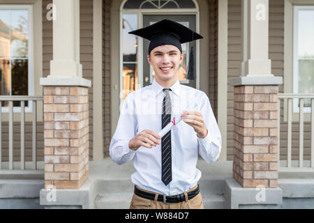 Giovani studenti di sesso maschile in possesso di un diploma indossando un cappello di graduazione di fronte a una casa. Foto Stock