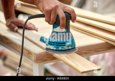 Macinacaffè lavoratore lucidi di una tavola di legno. Schede di levigatura orbitale macchina eccentrico. Foto Stock