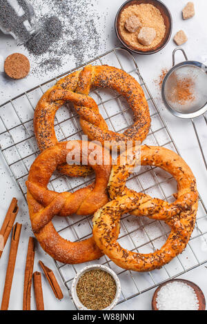 Pretzel. Pane appena sfornato pretzel con lo zucchero e i semi di papavero, cannella e cumino. Deliziosi dolci fatti in casa e dolci salati e gli ingredienti sul tavolo. Foto Stock