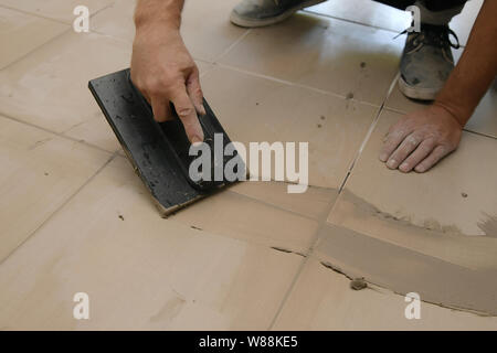 Lavoratore mettendo fugue su piastrelle sul pavimento nel corridoio. Sigillatura delle fughe di piastrelle ceramiche, close up Foto Stock