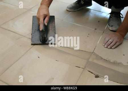 Lavoratore mettendo fugue su piastrelle sul pavimento nel corridoio. Sigillatura delle fughe di piastrelle ceramiche, close up Foto Stock