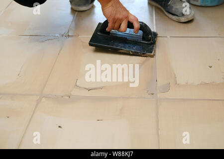 Lavoratore mettendo fugue su piastrelle sul pavimento nel corridoio. Sigillatura delle fughe di piastrelle ceramiche, close up Foto Stock