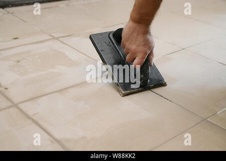 Lavoratore mettendo fugue su piastrelle sul pavimento nel corridoio. Sigillatura delle fughe di piastrelle ceramiche, close up Foto Stock