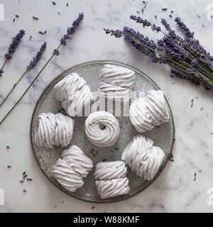 Laici piatta con una piastra di fatti in casa a base di marshmallows (zephyr, meringue) realizzato con lavanda su bianco marmor sfondo di pietra Foto Stock